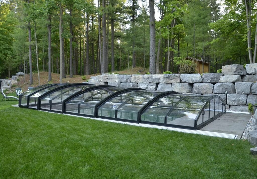 Medium height retractable pool cover covering outdoor pool on grassy lawn with chairs in the background.